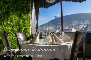 Un restaurante con una mesa dispuesta para comer, vista a un paisaje urbano y una pared verde.