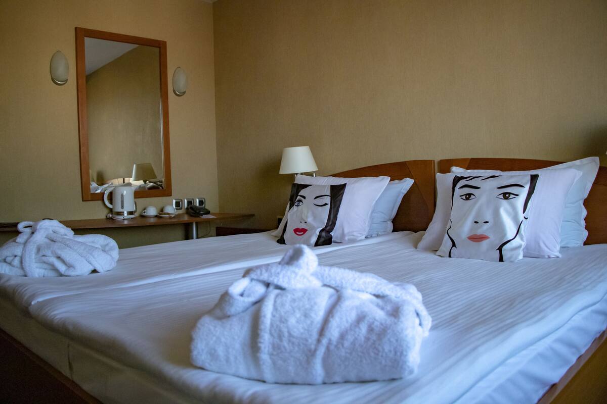 A hotel room with a large bed, two pillows with face designs, a bedside table with a lamp, and two towels on the bed.