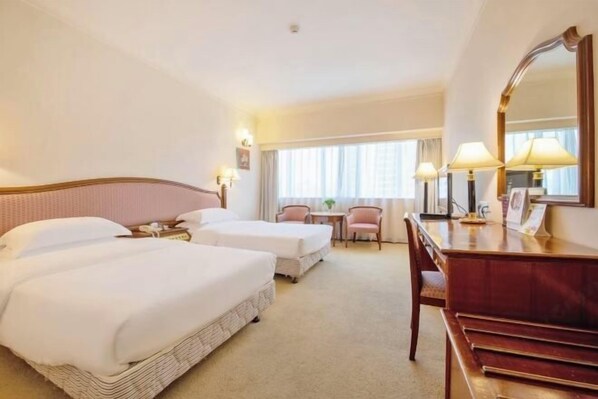Habitación de hotel con dos camas, un escritorio, una silla, un espejo y una ventana con cortinas.