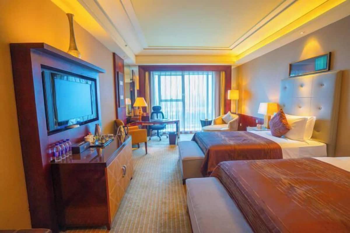 Ein Hotelzimmer mit Fernseher, Schreibtisch, zwei Betten und einem großen Fenster.