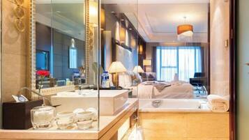 A modern hotel room with a large mirror, a bathtub, a vanity with toiletries, and a bed with a headboard.