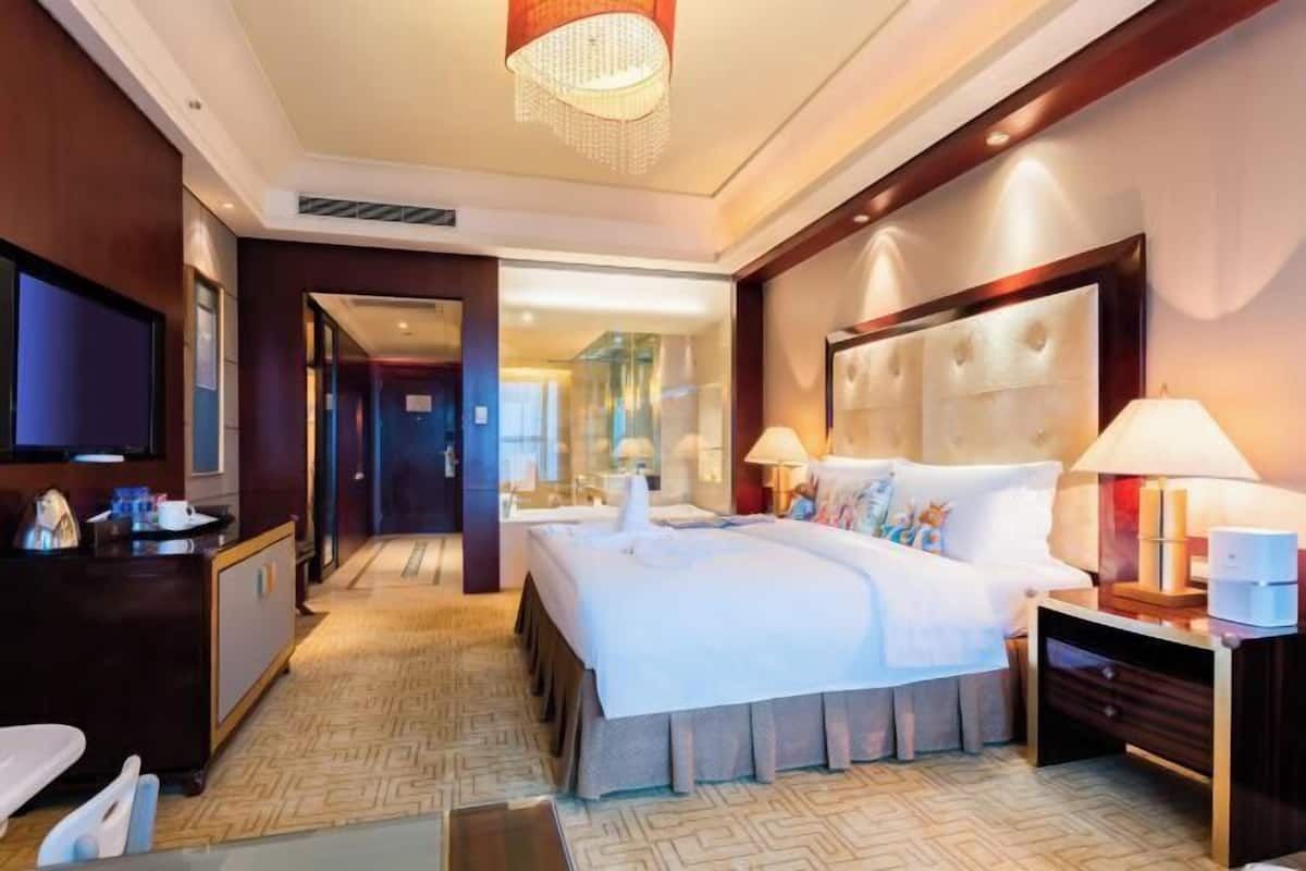 Ein Hotelzimmer mit einem großen Bett, Nachttischlampen, einem Fernseher und einem Schreibtisch mit Stuhl.