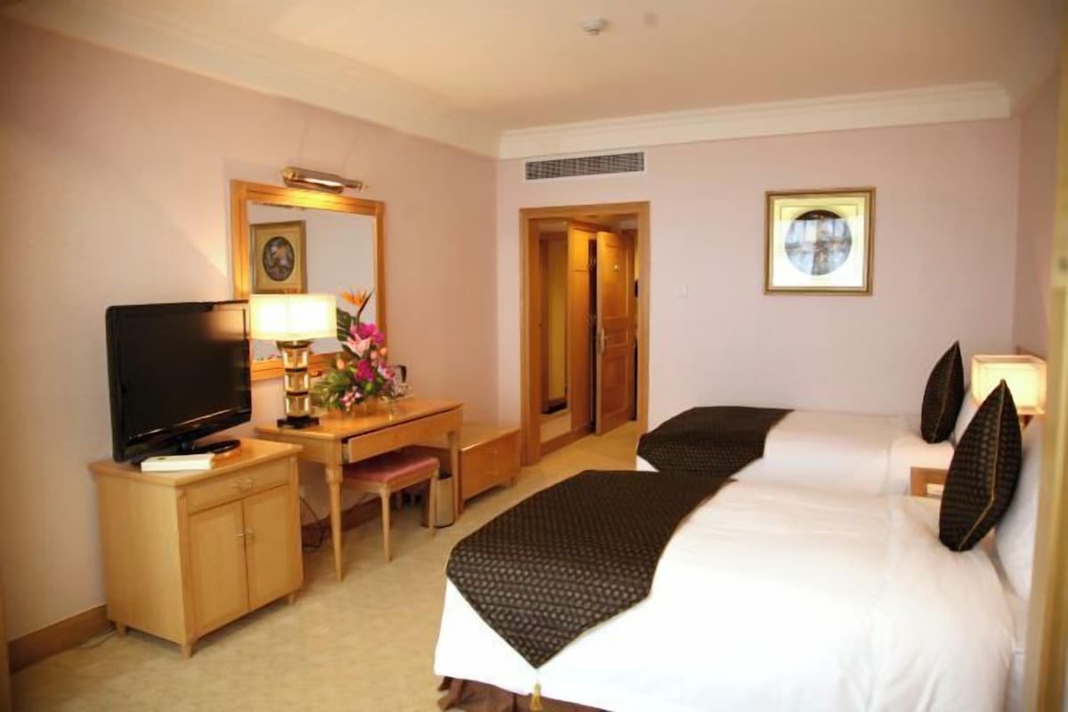 Una habitación de hotel con una cama, un escritorio con televisor, una silla y una puerta que da a otra habitación.