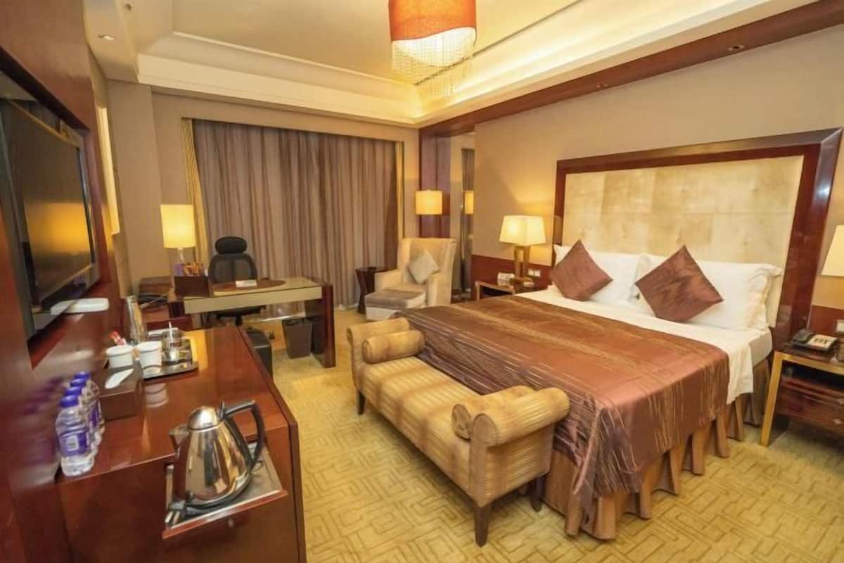 Ein Hotelzimmer mit einem großen Bett, einem Schreibtisch mit Stuhl, einer Couch, einem Fernseher und einer Minibar.