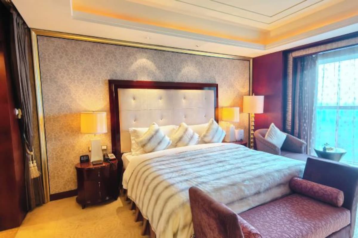 Una habitación de hotel con una cama grande, dos mesitas de noche, una silla y una ventana con cortinas.