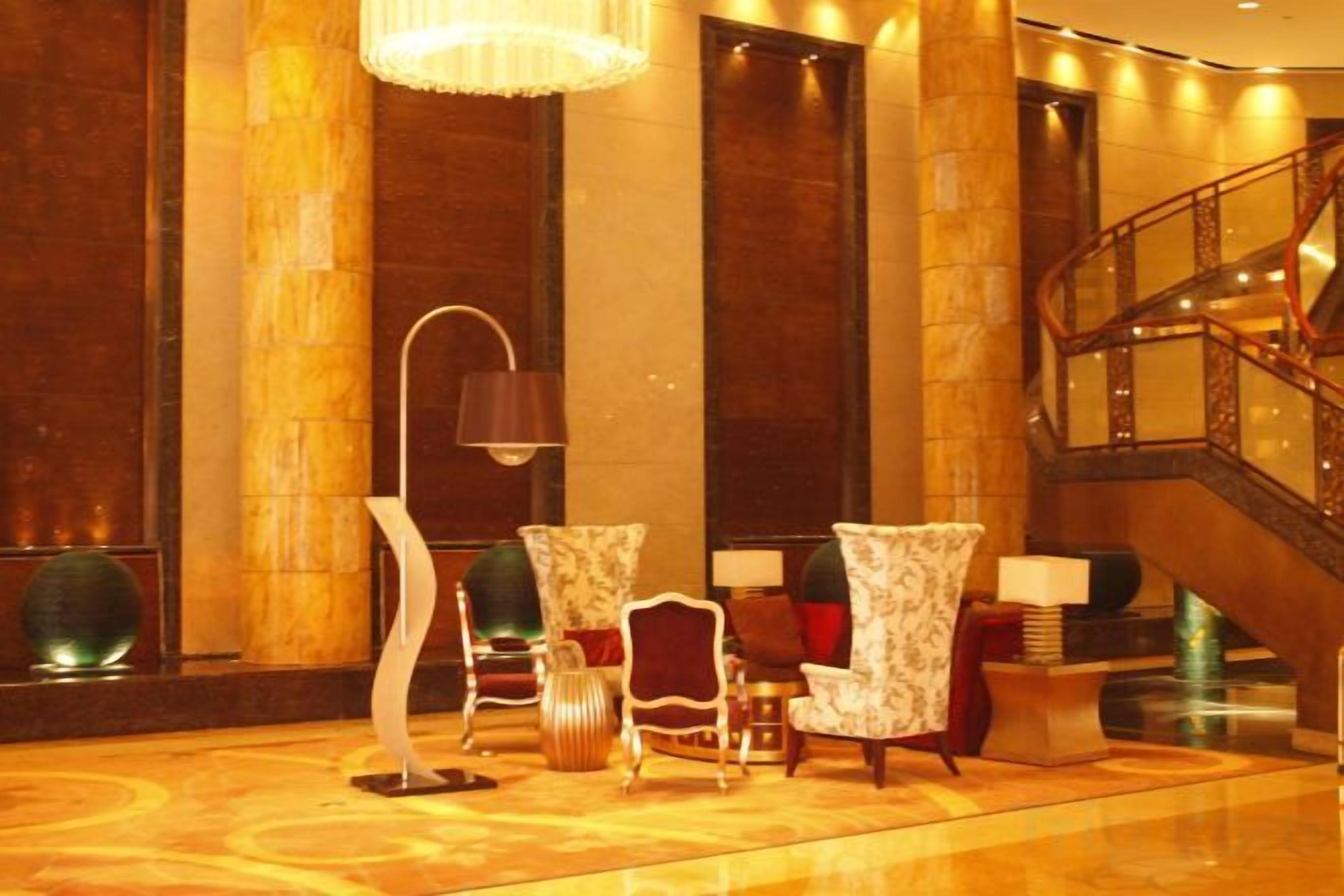 A lobby with a grand staircase, elegant chairs, and a modern floor lamp.
