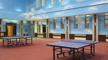 Una habitación con dos mesas de ping pong, amplias ventanas y piso cubierto de alfombra roja.