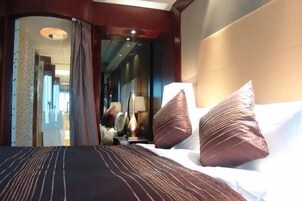 Habitación de hotel con una cama grande, dos almohadas, una mesita de noche, una lámpara y vistas al pasillo.