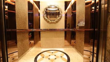 An elevator interior with a central mirror, a handrail, and a patterned floor.