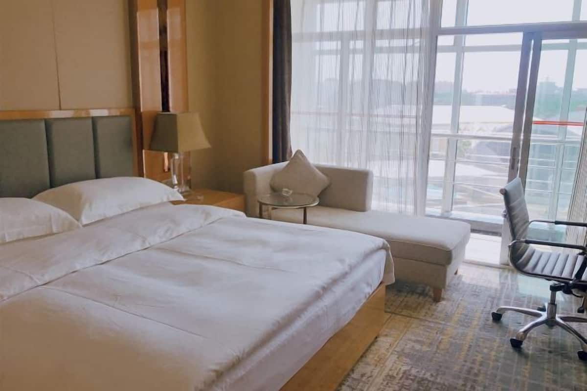 Ein Hotelzimmer mit einem großen Bett, einem kleinen Sofa, einem Sessel und Blick durch große Fenster.