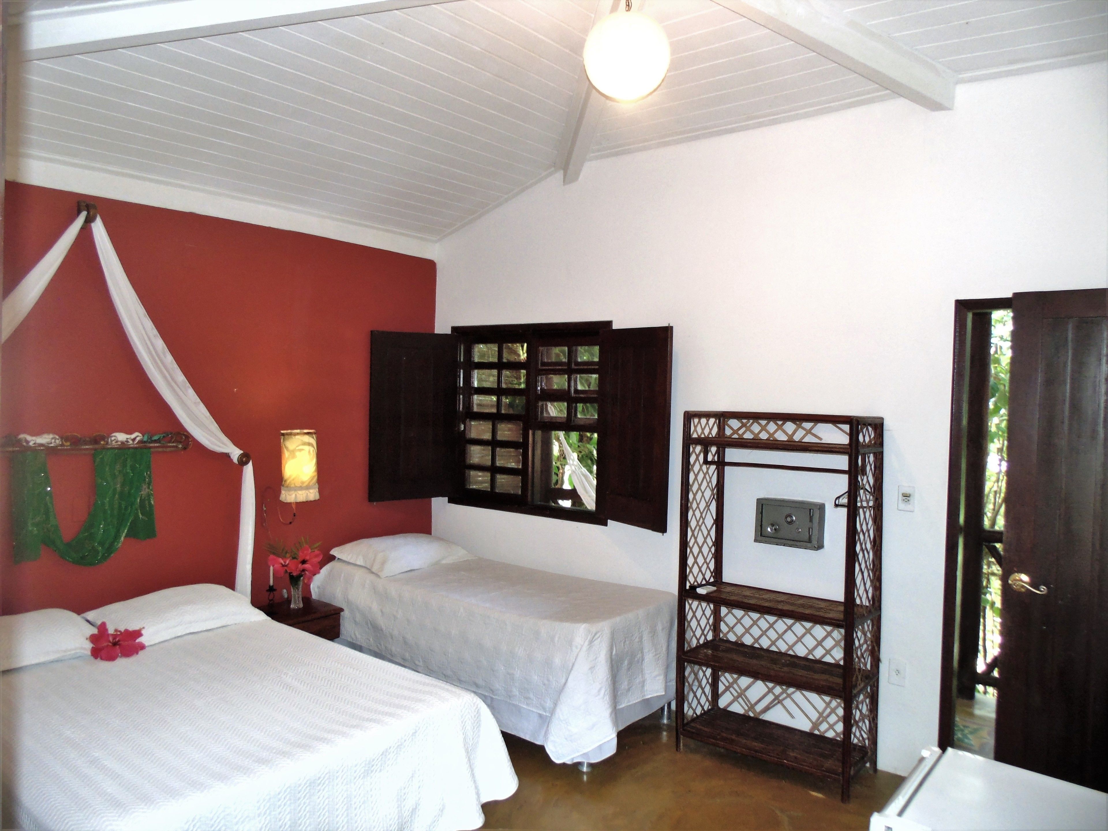 A room with two beds, a wooden shelf, a window with shutters, and a door.