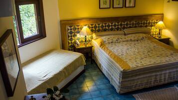 Una habitación con una cama, una mesita de noche con lámpara, una pequeña mesa con un florero y una ventana.