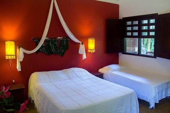 Una habitación con una cama y una cama más pequeña, ambas cubiertas con ropa blanca. Hay dos lámparas de pared a cada lado de la cama.