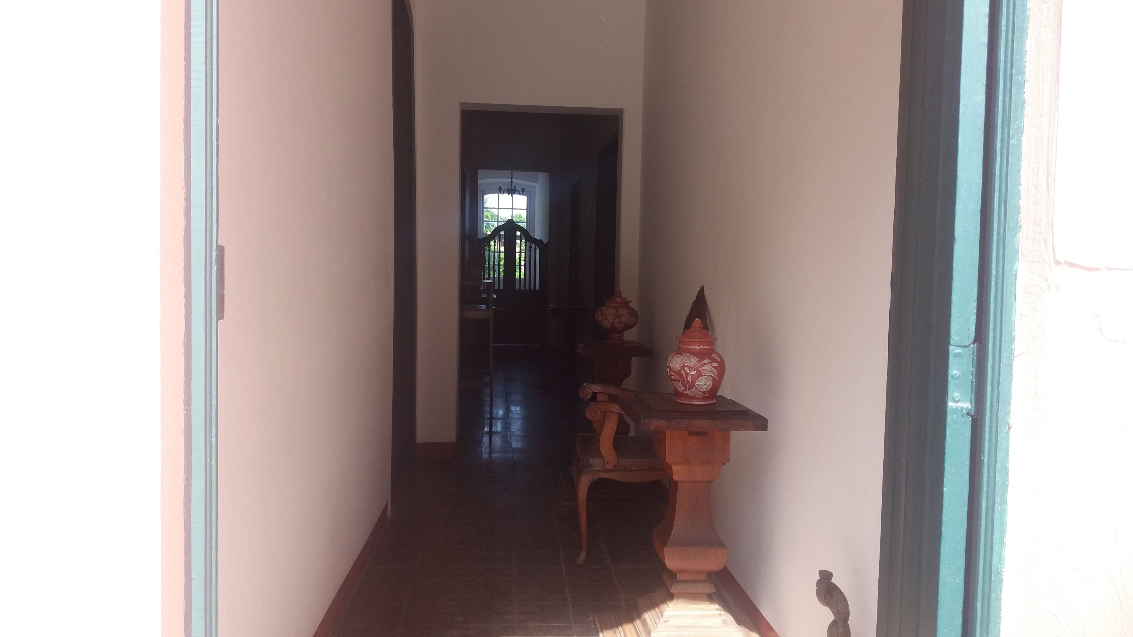 A narrow hallway with a wooden bench and a decorative vase. A door leads to a brighter room with a view of the outdoors.