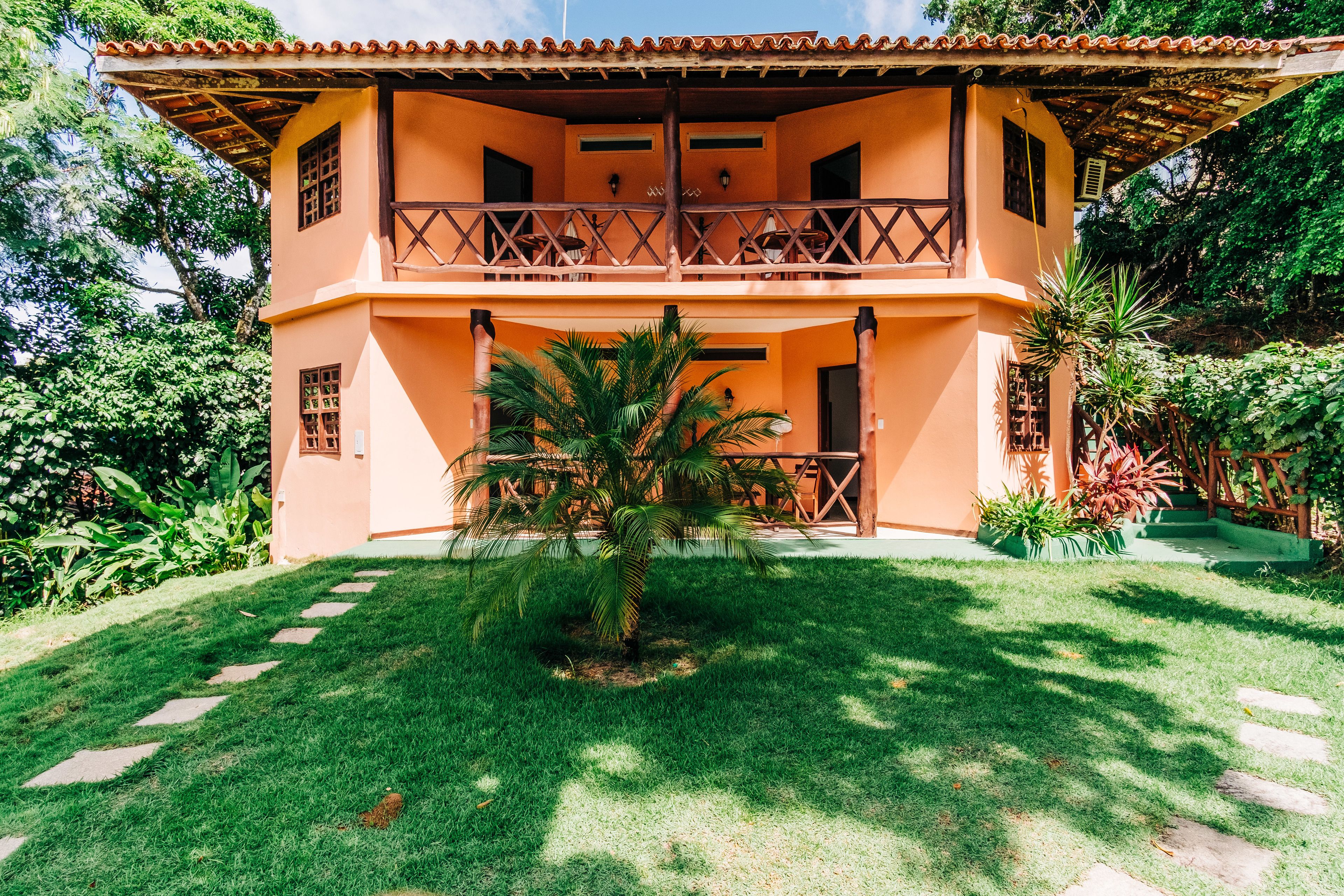 Un edificio de dos pisos con un balcón y una palmera pequeña en el jardín delantero.