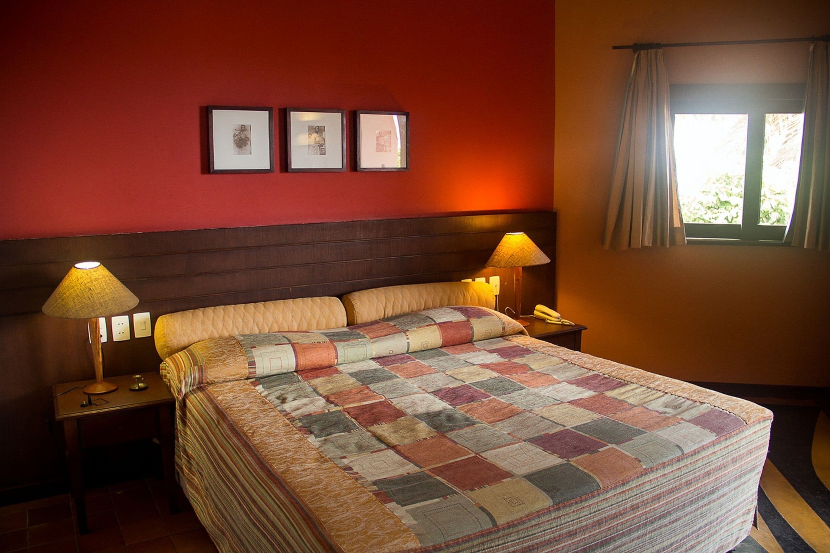 A neatly made bed with a checkered quilt, two bedside lamps, and framed pictures on the wall.