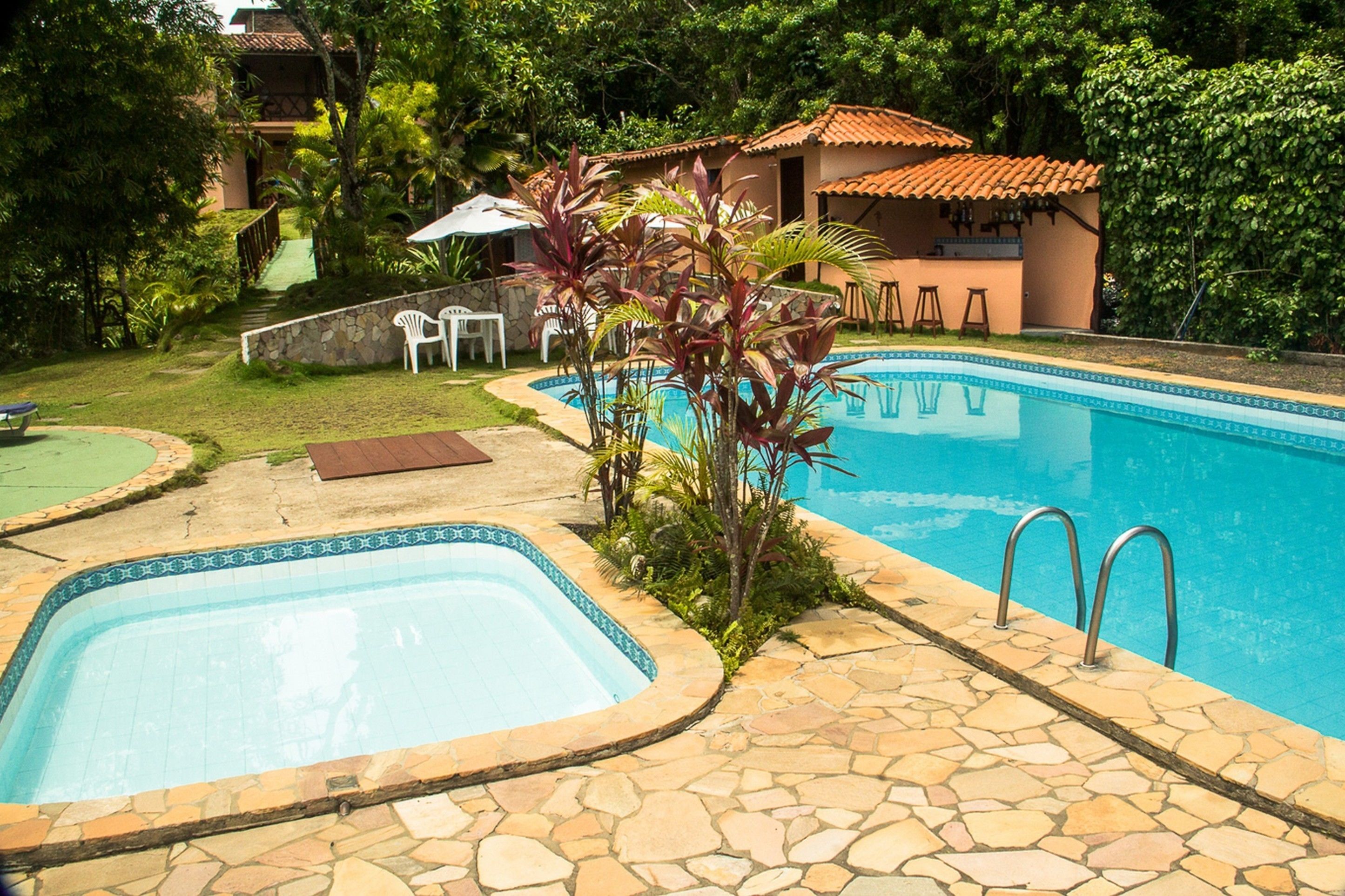 A swimming pool with stone tiles, a bar area, and a small outdoor seating area with chairs and a table.