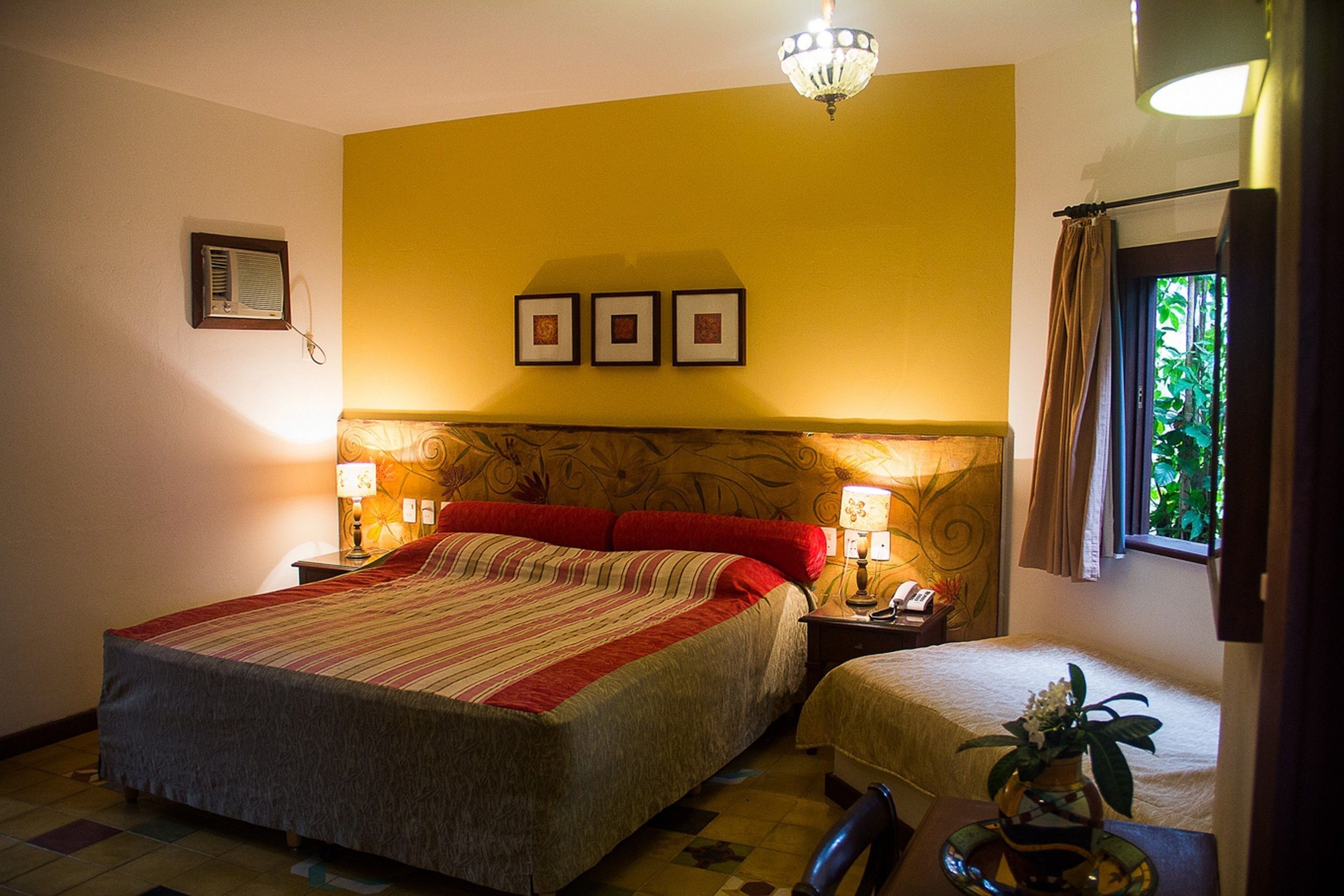 A hotel room with a large bed, two bedside tables with lamps, a small table with a vase, and a window with curtains.