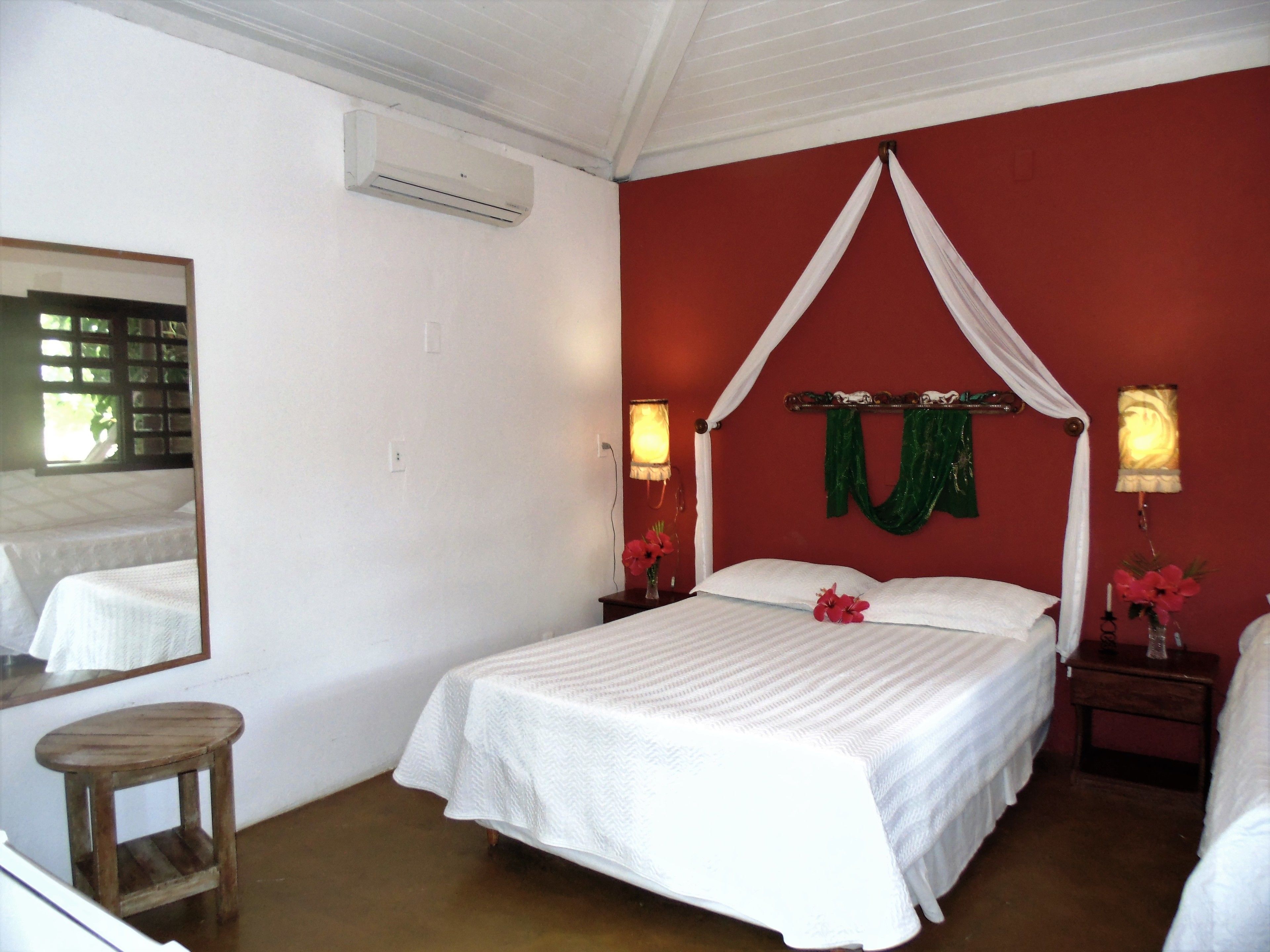 Quarto com cama, mesa de cabeceira, espelho e ar condicionado.