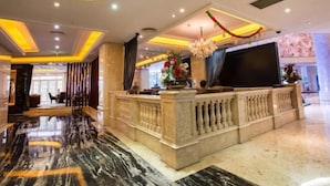 A hotel lobby with a marble reception desk, a chandelier, and a large flat-screen TV. - Sanbu Holiday Hotel (Jiangmen)