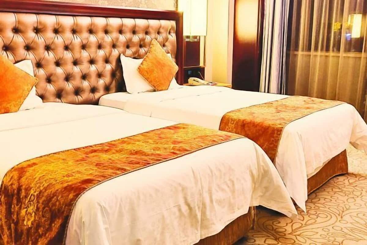 Hotellihuone, jossa on kaksi sänkyä, napitettu pääty ja kuvioitu matto.