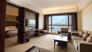 A hotel room with a bed, a TV, a sofa, a coffee table, and a large window with a view of the sea. - Sanbu Holiday Hotel (Jiangmen)