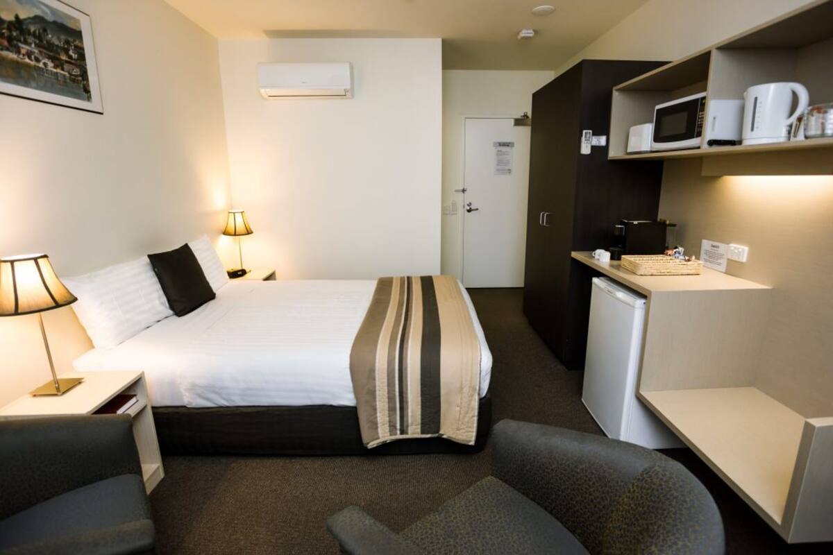 A hotel room with a bed, bedside lamps, a desk, a microwave, and a coffee maker.
