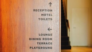 A wooden reception desk with directional arrows pointing to various hotel amenities including the reception, motel toilets, lounge, dining room, terrace, and playground. - Shoreline Hotel (Howrah)