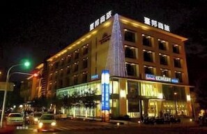 A multi-story hotel with a prominent triangular structure on the corner, illuminated signage, and a street view with vehicles. - Taipung Suites (Tainan)