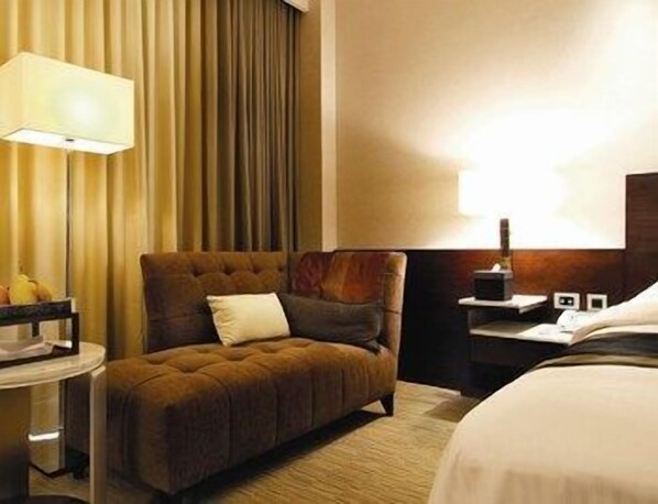 A hotel room with a bed, a brown armchair, a small table with a lamp, and a nightstand.