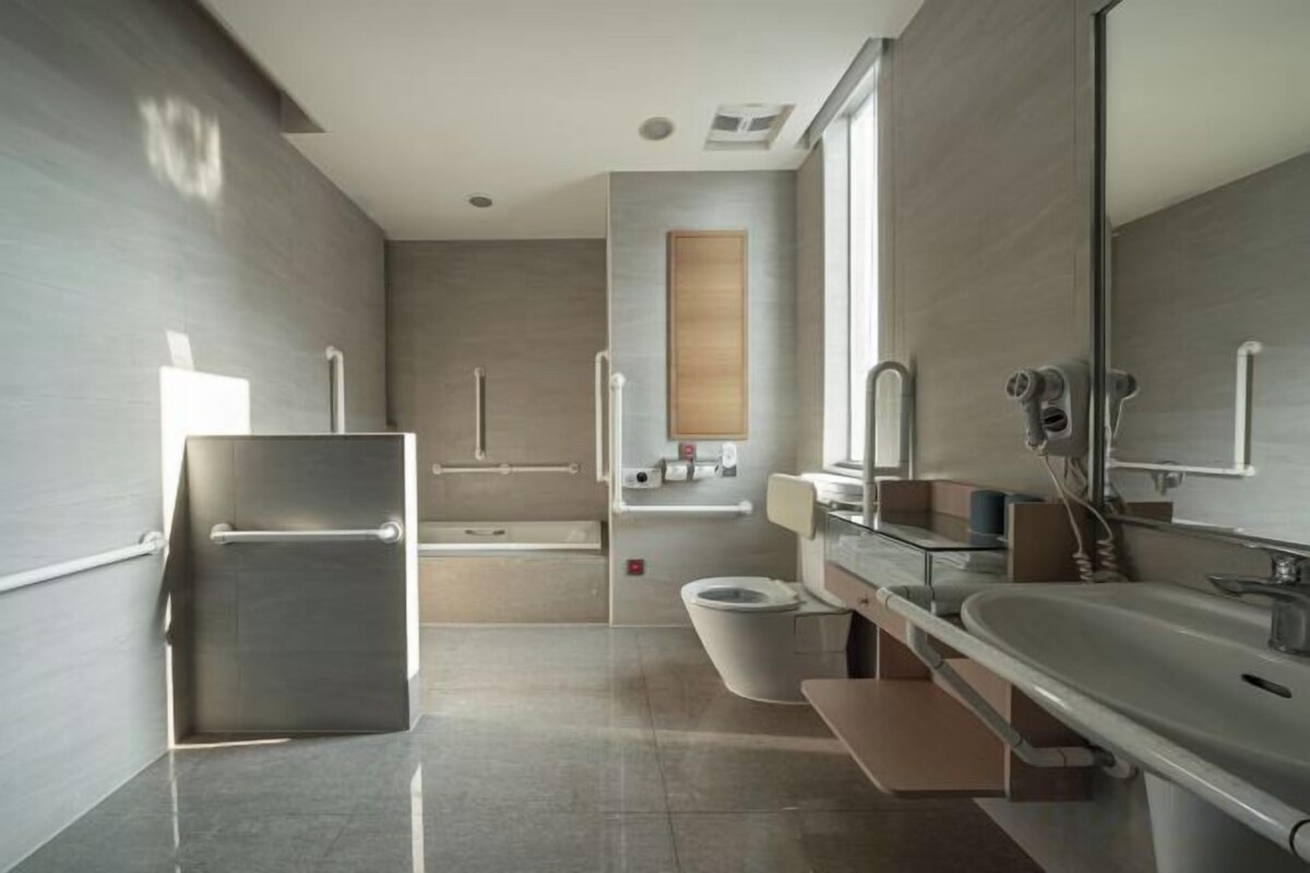 A modern bathroom with a large mirror, a bathtub, and a toilet.