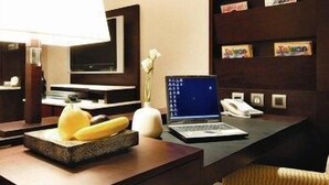 A hotel reception desk with a laptop, a telephone, a decorative vase, and a fruit bowl.