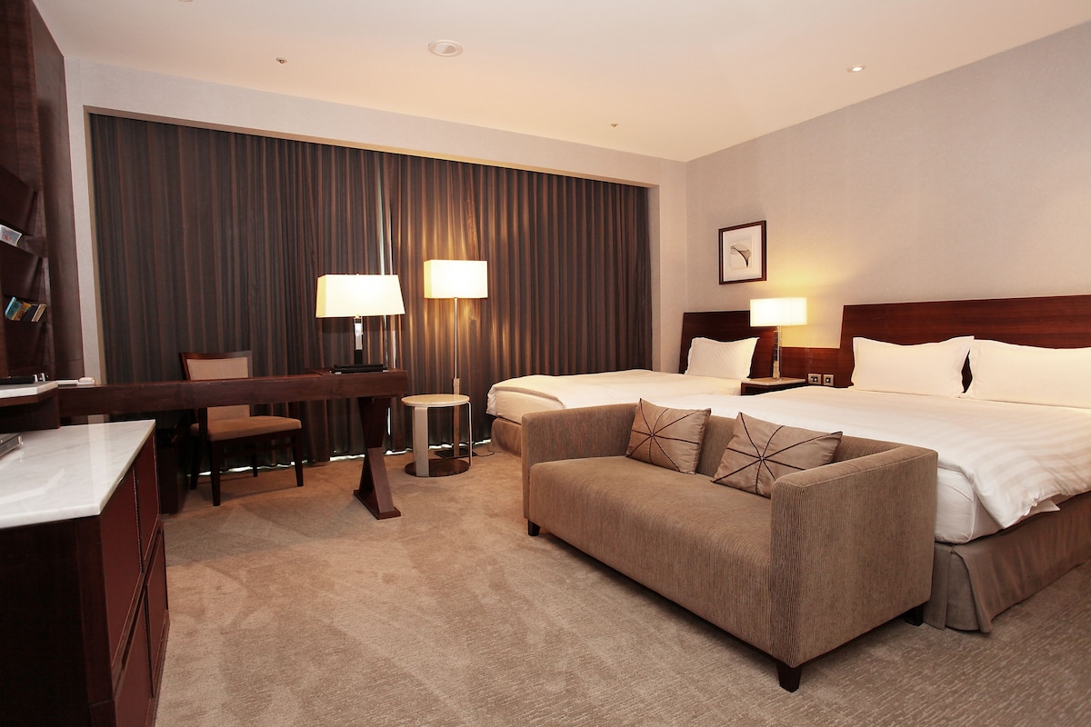 Una habitación de hotel con cama, dos mesitas de noche con lámparas, un sofá, un escritorio y una silla.