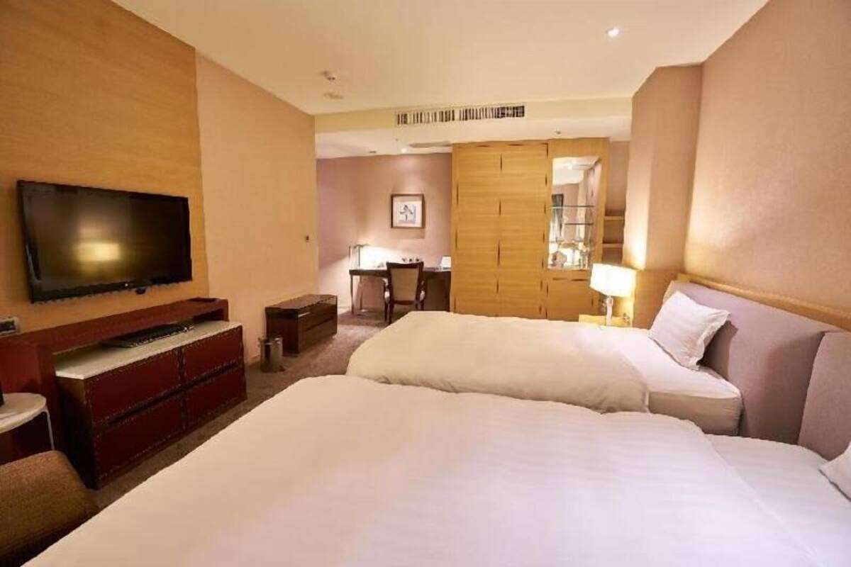 Quarto de hotel com televisão, secretária, guarda-roupa e duas camas.