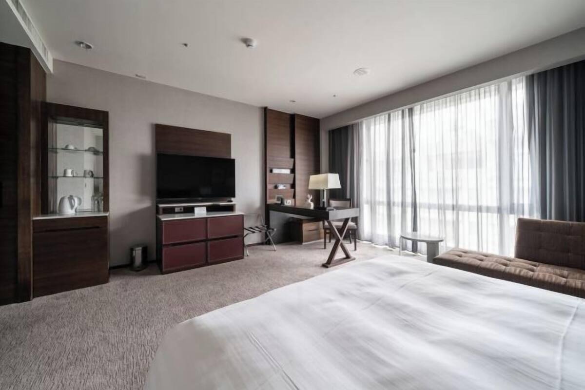 Quarto de hotel moderno com uma cama grande, televisão, escrivaninha e sofá.