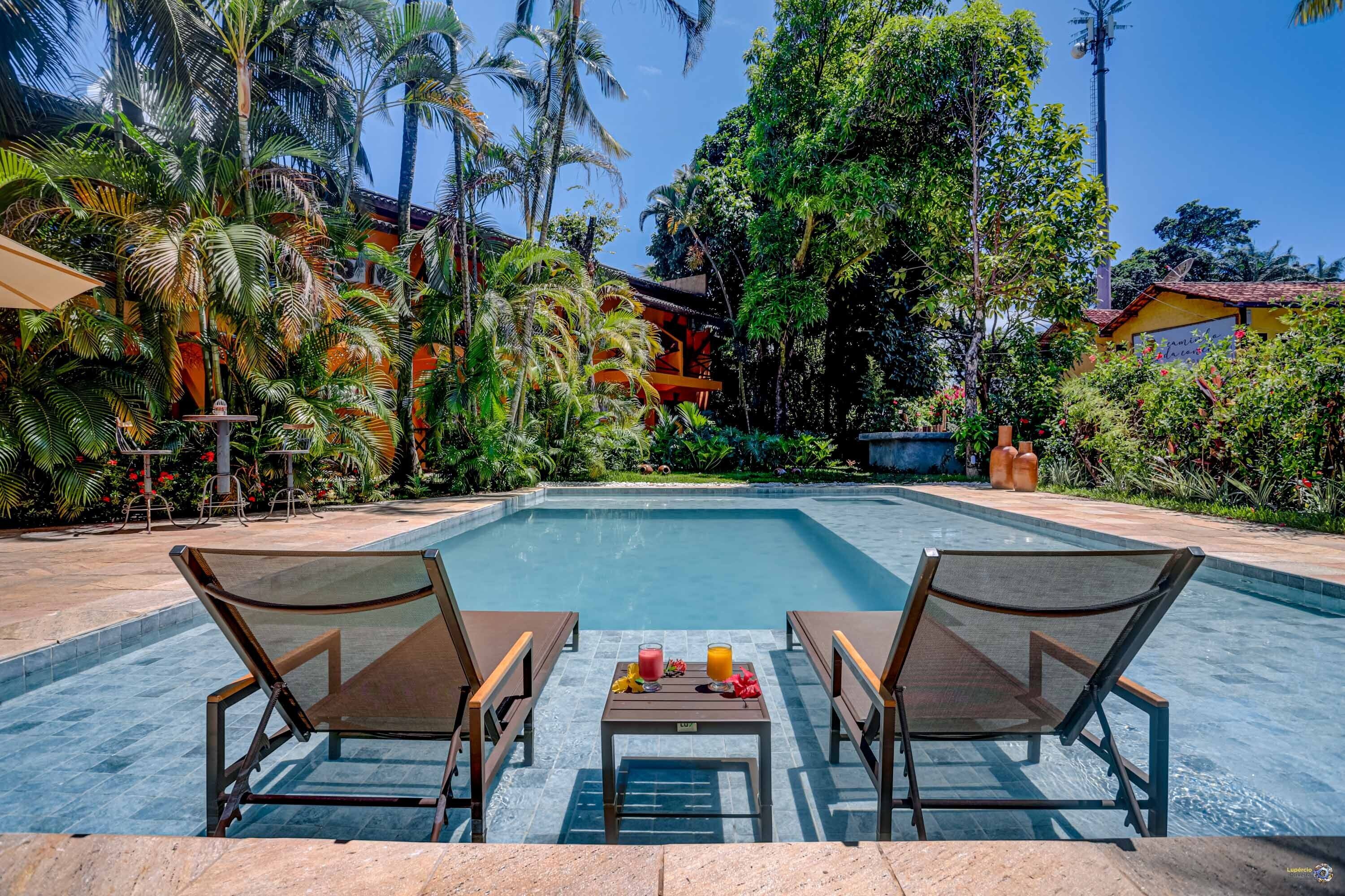 A swimming pool with lounge chairs and a table, surrounded by lush greenery and palm trees.