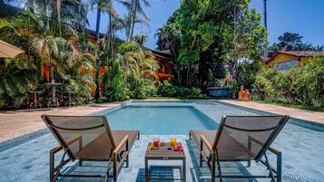 A swimming pool with lounge chairs and a table, surrounded by lush greenery and palm trees.