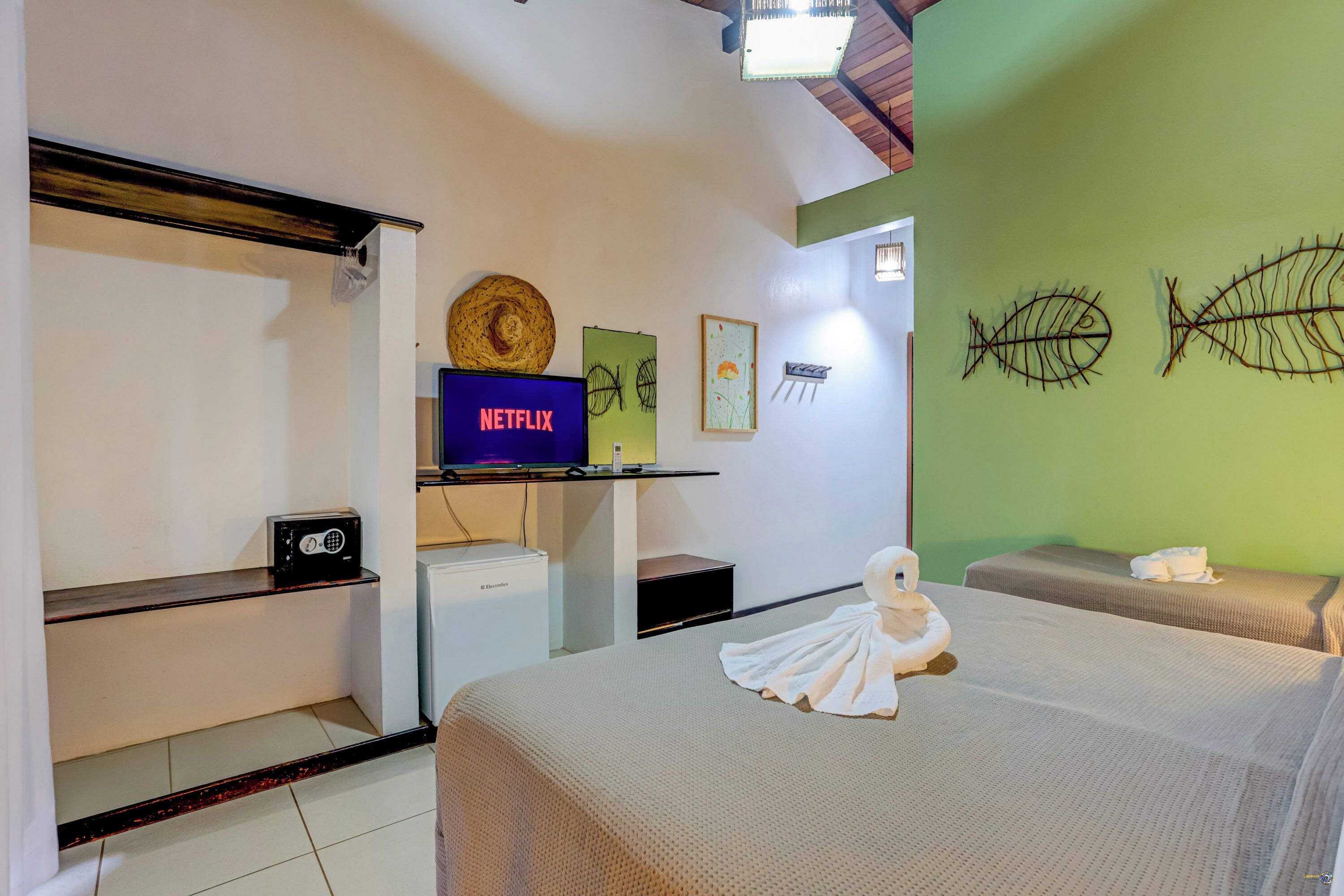 Ein Hotelzimmer mit einem Bett, einem Fernseher, der 'NETFLIX' anzeigt, einem kleinen Schreibtisch mit einem Computer und einer Wand mit Fischskelett-Dekorationen.