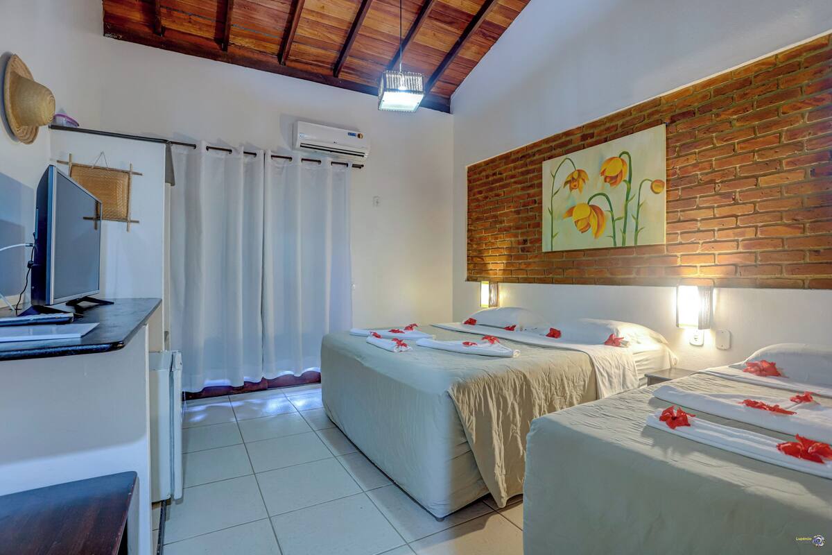 Habitación de hotel con dos camas, un escritorio con computadora, aire acondicionado y un cuadro en la pared.