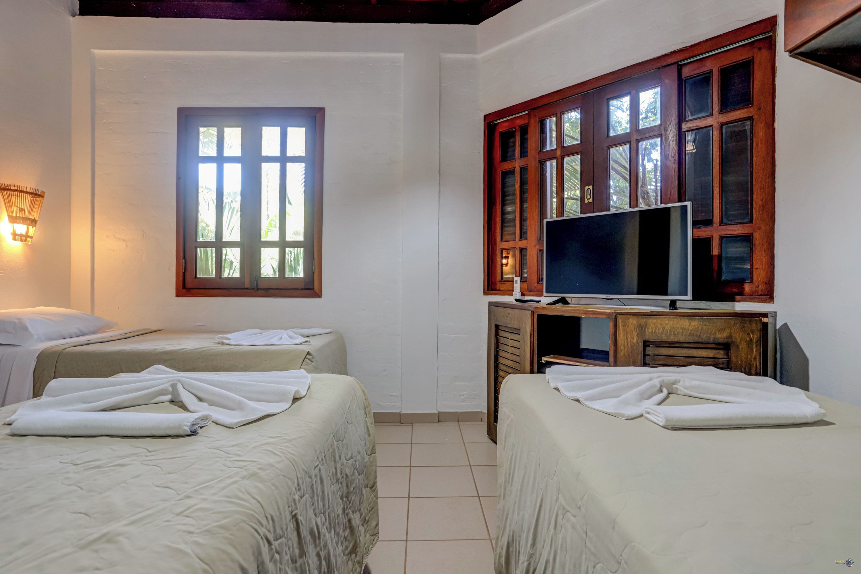 Habitación de hotel con dos camas, un televisor y ventana con vista a follaje.