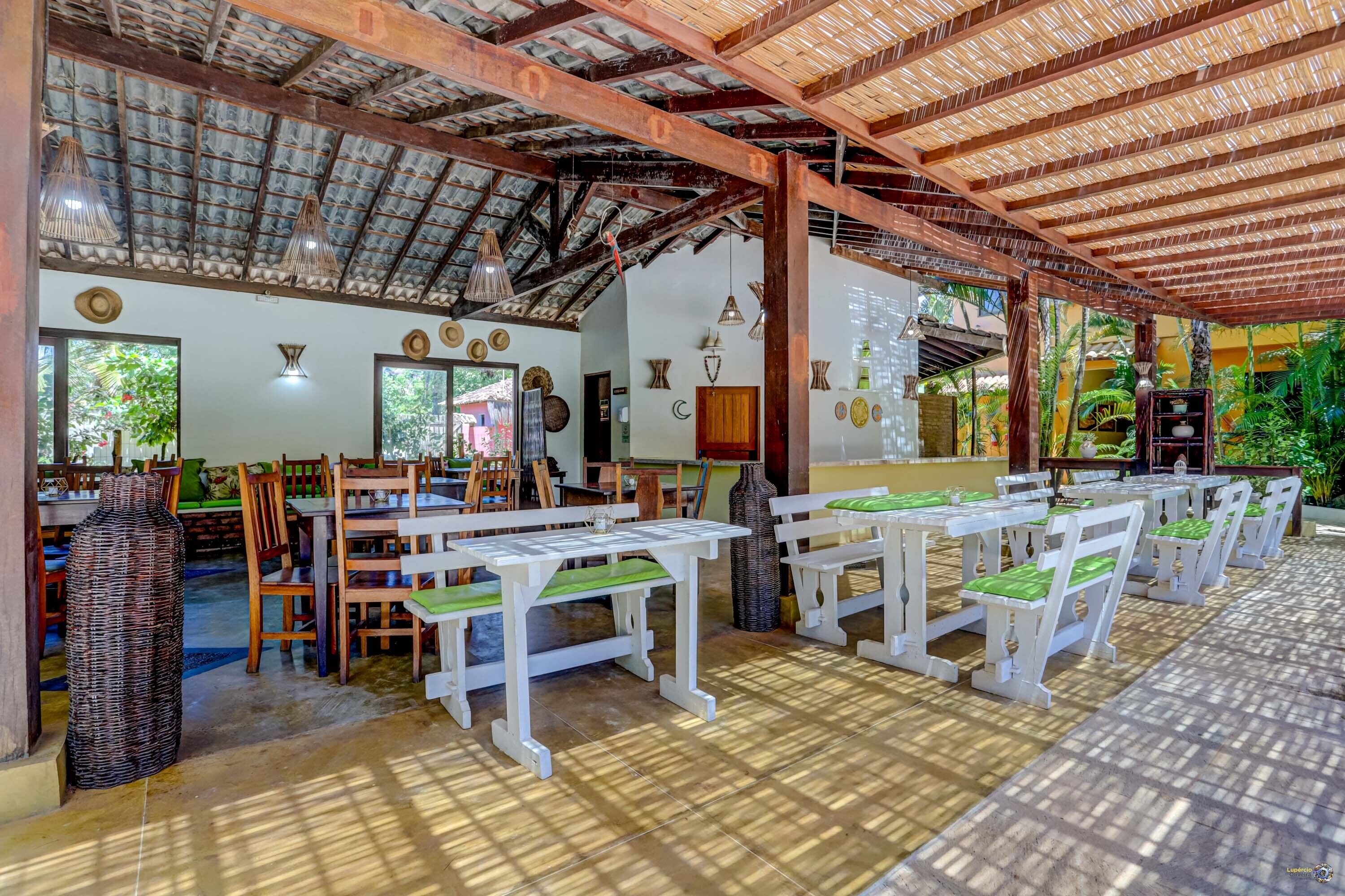 A covered outdoor dining area with tables and chairs, a thatched roof, and natural light.