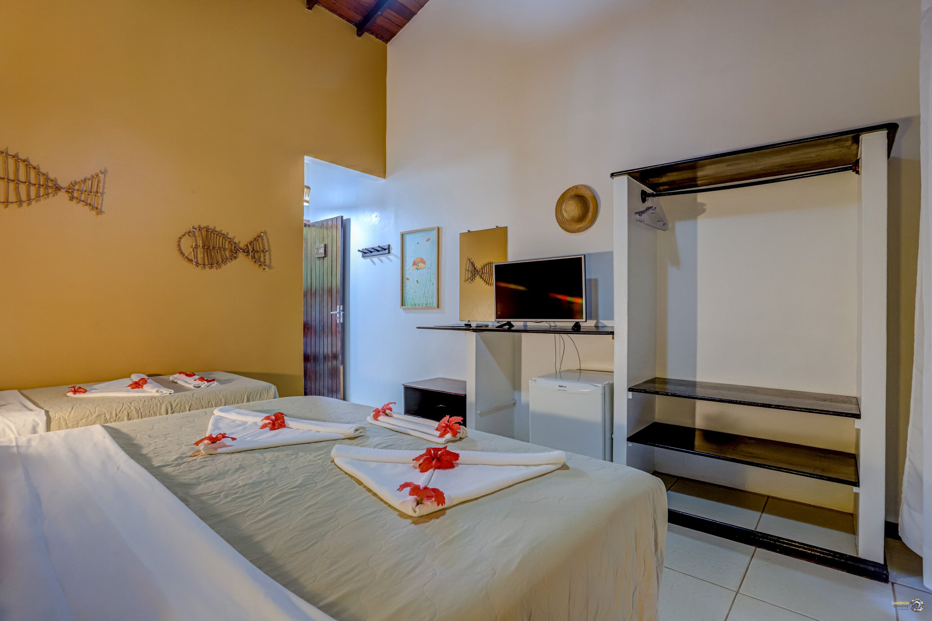A hotel room with two beds, a TV, a shelf, and artwork on the walls.