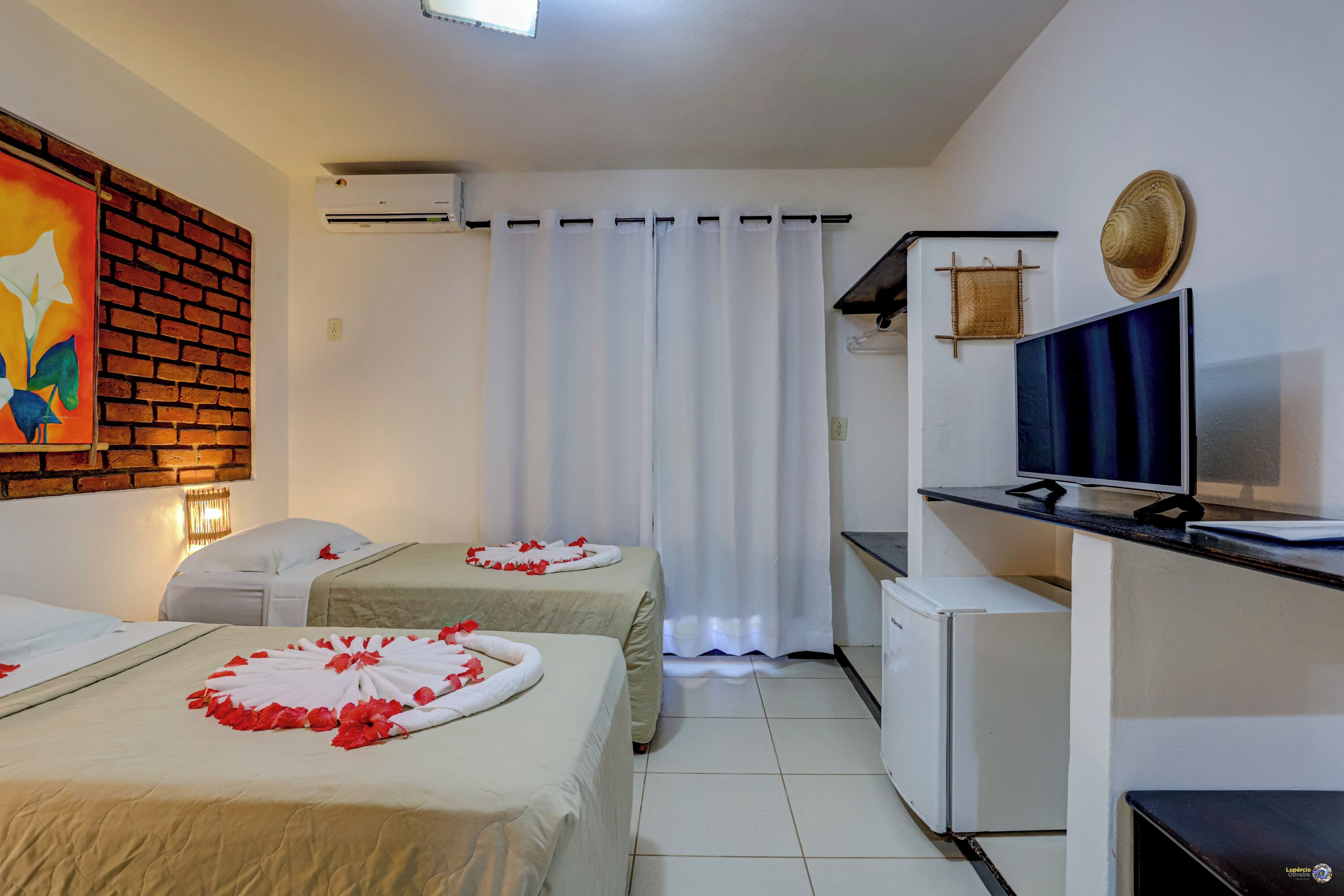 A hotel room with two beds, a TV, a small fridge, and a brick wall with a painting.