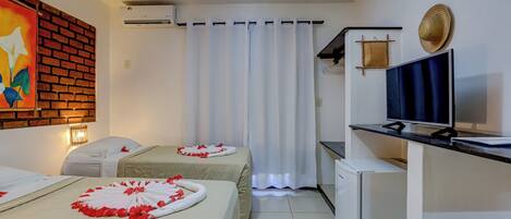 A hotel room with two beds, a TV, a small fridge, and a brick wall with a painting.