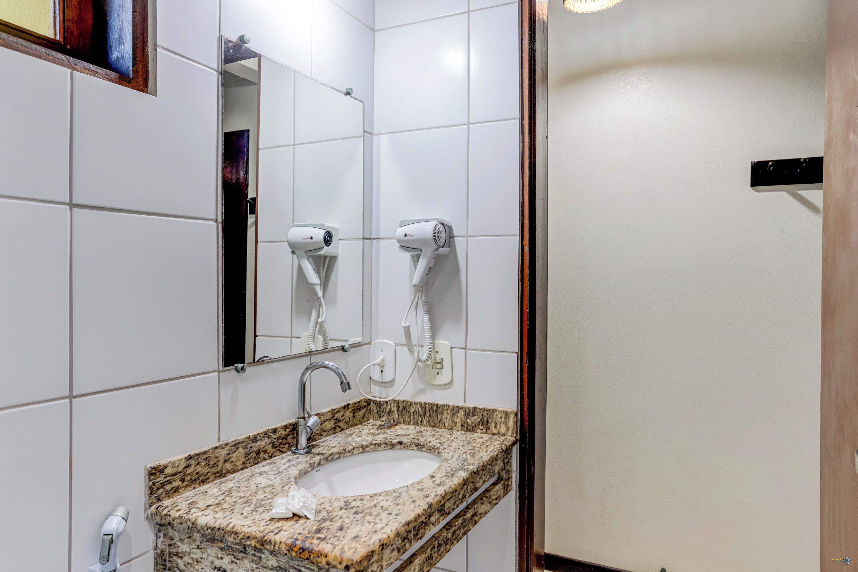 Une salle de bain avec un lavabo en granit, deux sèche-cheveux fixés au mur et un miroir au-dessus du lavabo.