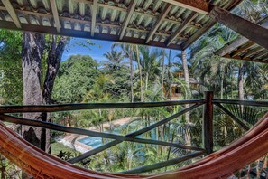 Una hamaca bajo una pérgola de madera con vista a una piscina y vegetación tropical.