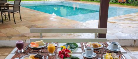 A breakfast setup with various dishes and beverages on a table, overlooking a swimming pool.