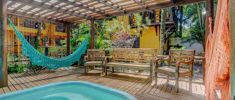 Una terraza de madera con piscina, bancos y una hamaca.