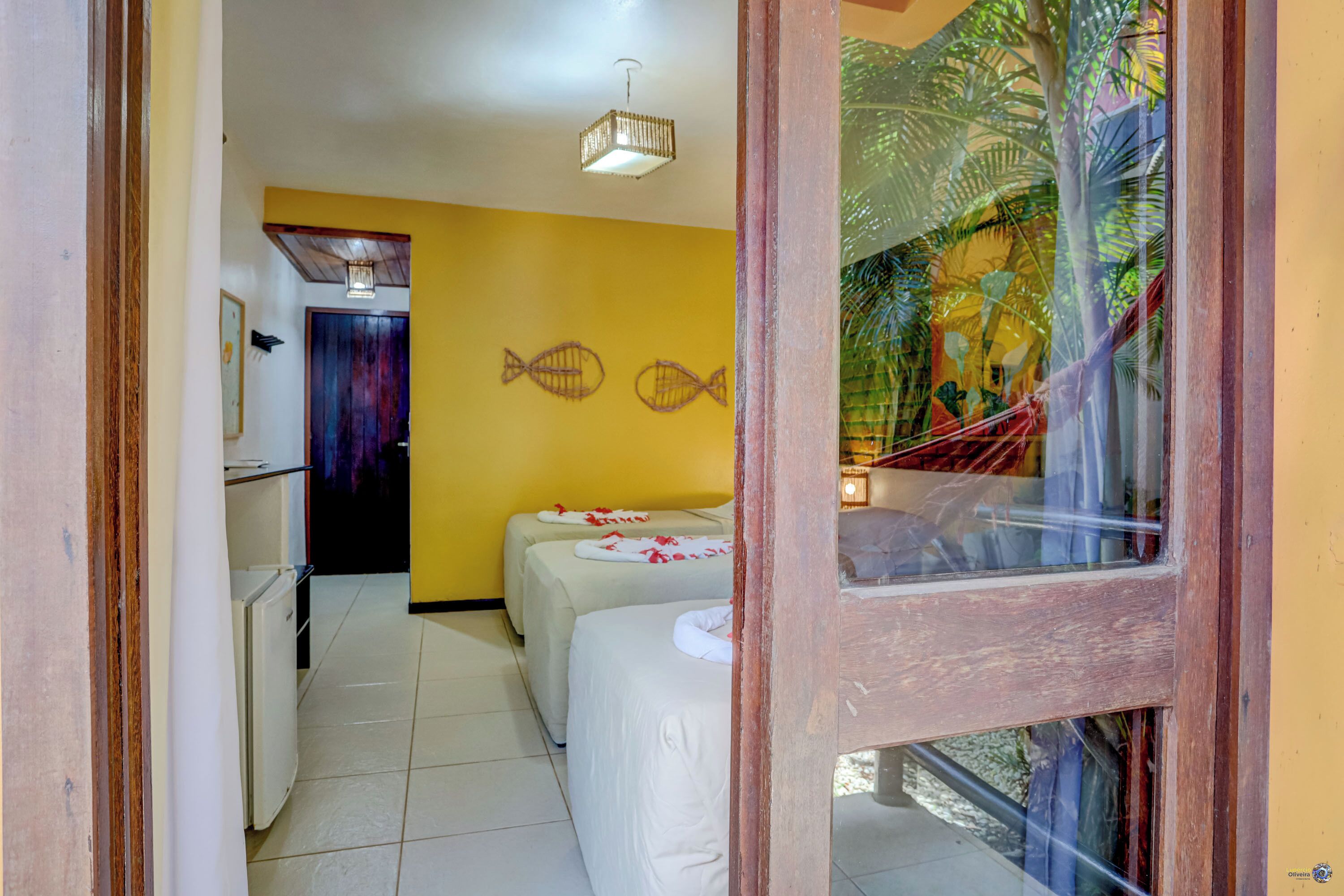 A hotel room with two beds, a small kitchenette, and a view of a palm tree through a window.