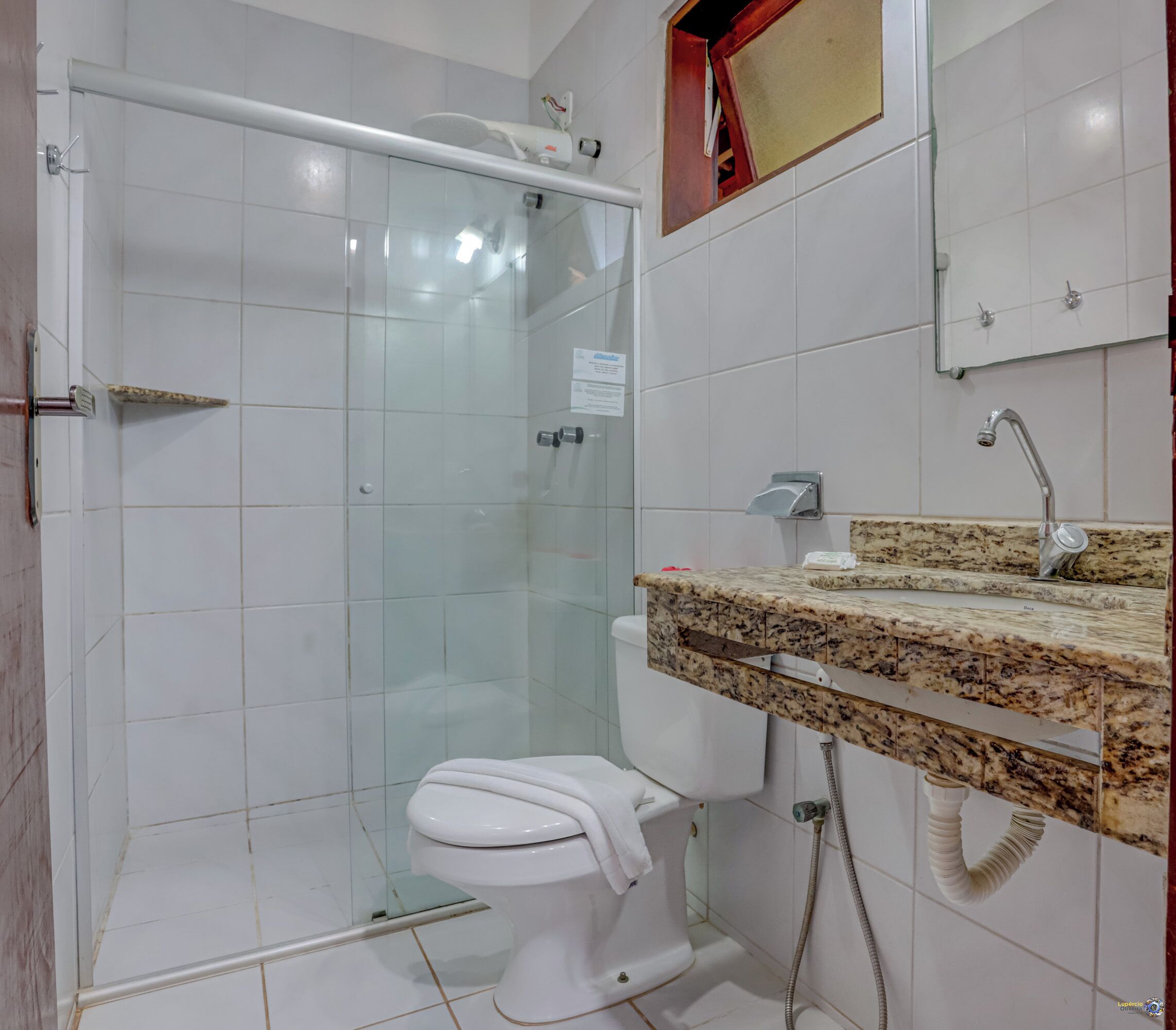 Un baño con ducha envuelta en vidrio, inodoro blanco y encimera de granito con lavabo.